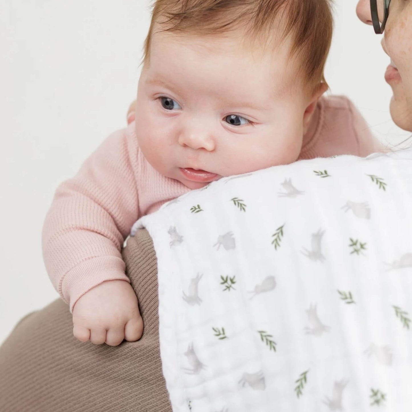 Baby resting on adult’s shoulder with Lulujo muslin burp cloth in bunny and fern print—soft, absorbent, and gentle on baby’s delicate skin.