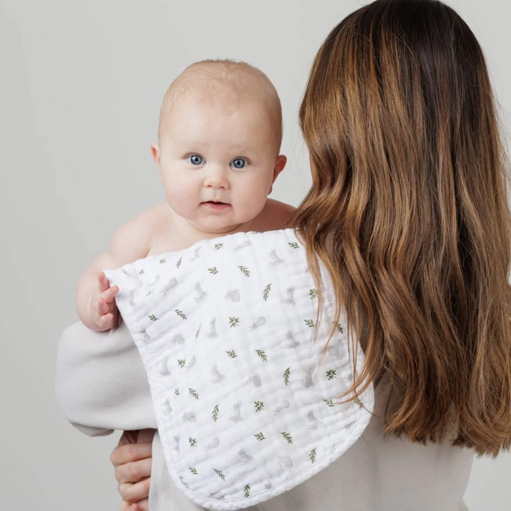 Mother holding baby over shoulder using Lulujo burp cloth in bunny and fern print—lightweight, curved shape with soft, triple-layer muslin.