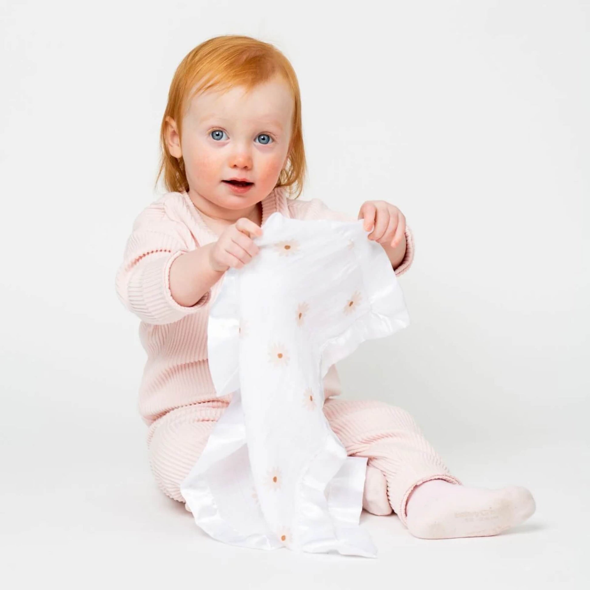 Baby holding Lulujo muslin security blanket with daisy print and satin trim—lightweight, breathable, and perfect for comfort on the go.