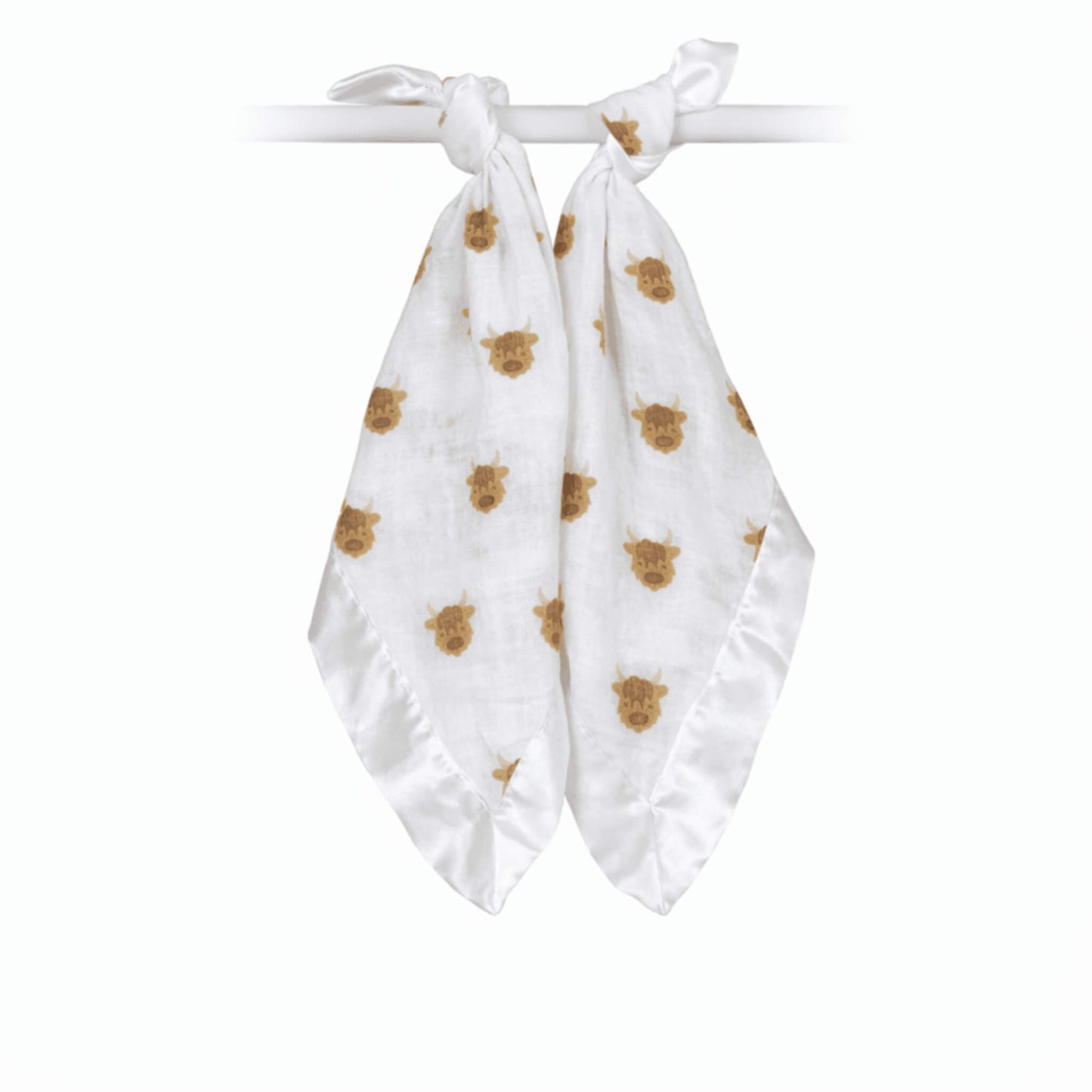 Two soft muslin comfort blankets tied onto a rail, featuring a repeating brown highland cow pattern with silky satin edging.