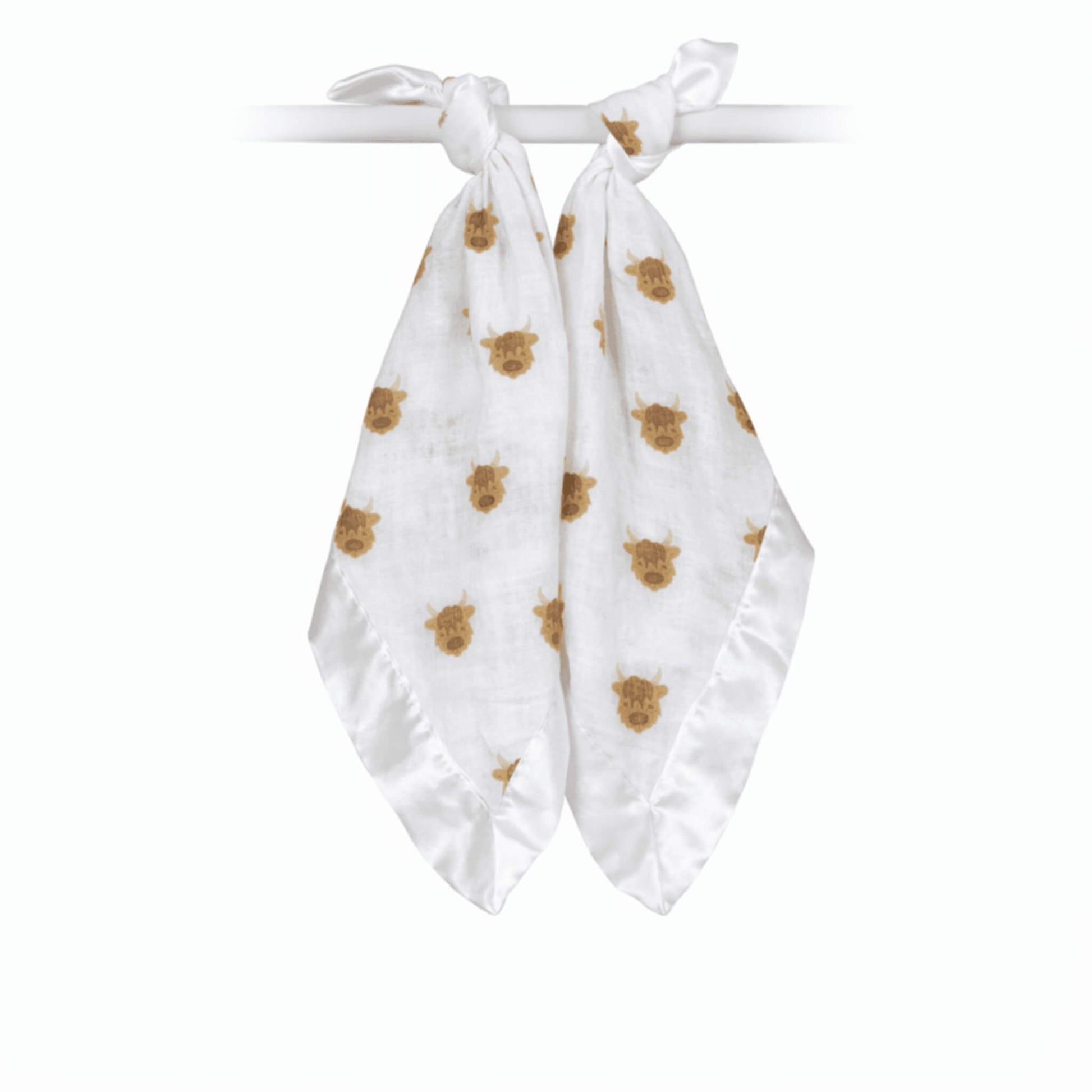 Two soft muslin comfort blankets tied onto a rail, featuring a repeating brown highland cow pattern with silky satin edging.