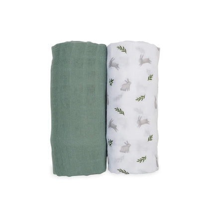 Two Lulujo Muslin Swaddles shown rolled side by side, one solid sage green and one white with soft grey bunny and green fern print.