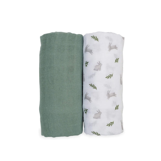 Two Lulujo Muslin Swaddles shown rolled side by side, one solid sage green and one white with soft grey bunny and green fern print.