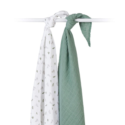 Two muslin swaddles knotted over a white rod, one plain green and one white printed with bunnies and green sprigs.