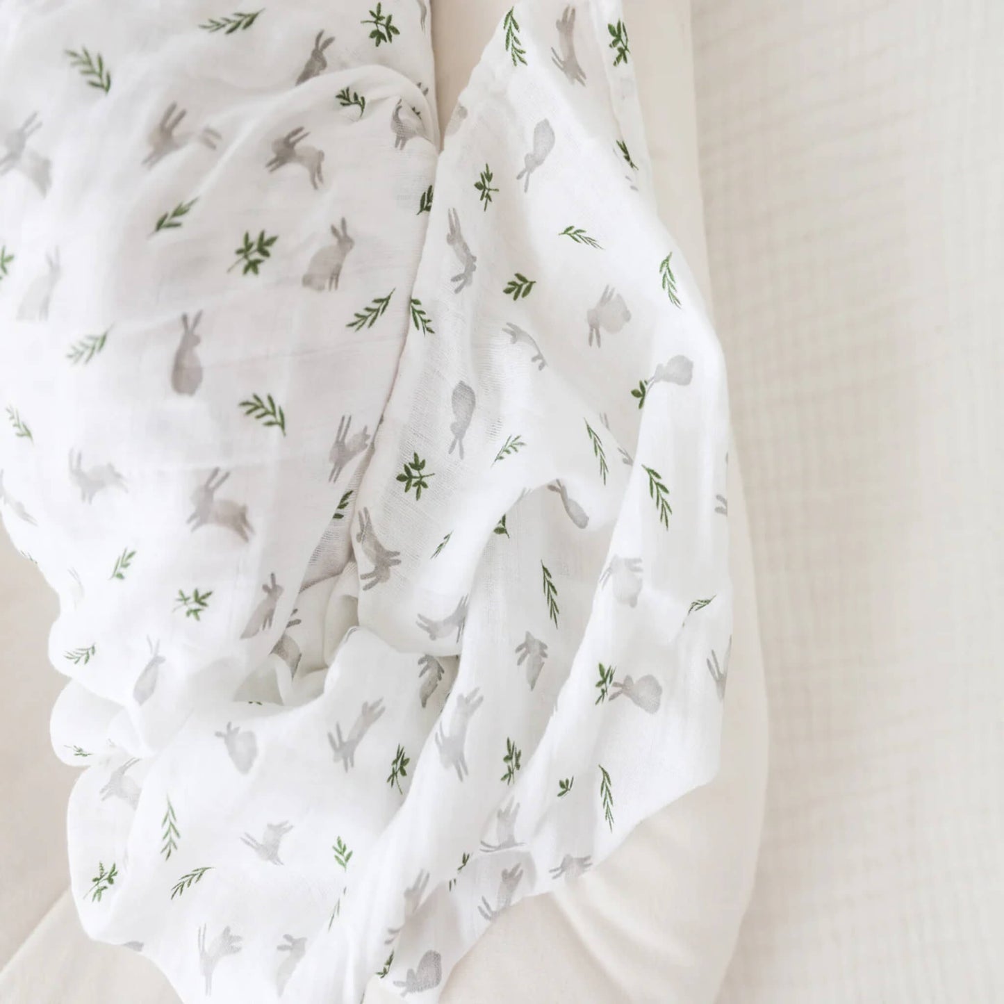 Close-up of soft white muslin fabric printed with small grey rabbits and delicate green leaves.
