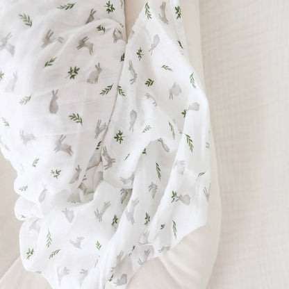 Close-up of soft white muslin fabric printed with small grey rabbits and delicate green leaves.