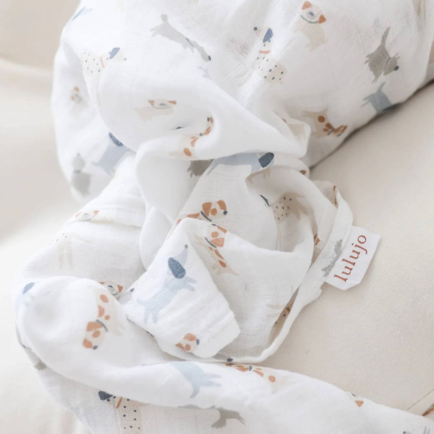 Close-up of soft white muslin fabric with small dog illustrations and a woven Lulujo tag visible.