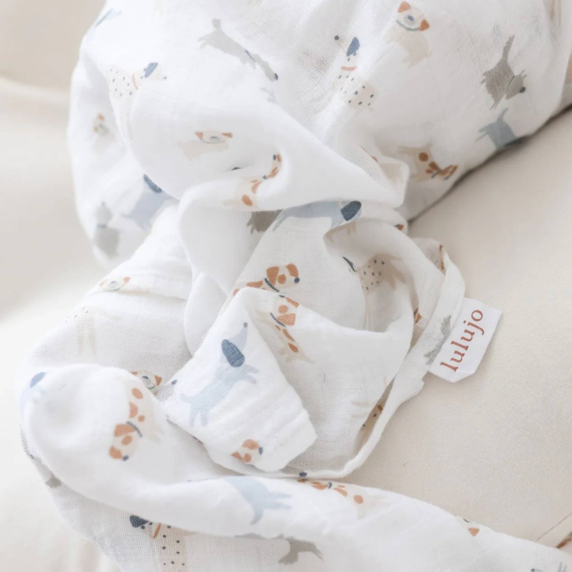 Close-up of soft white muslin fabric with small dog illustrations and a woven Lulujo tag visible.