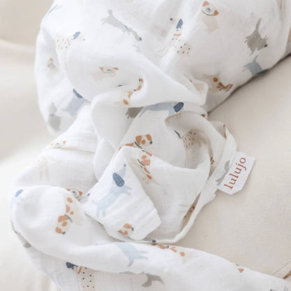 Close-up of soft white muslin fabric with small dog illustrations and a woven Lulujo tag visible.