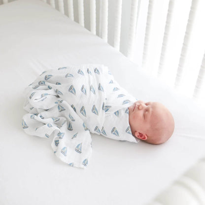 Sleeping baby swaddled in a white muslin blanket decorated with small blue sailboats.