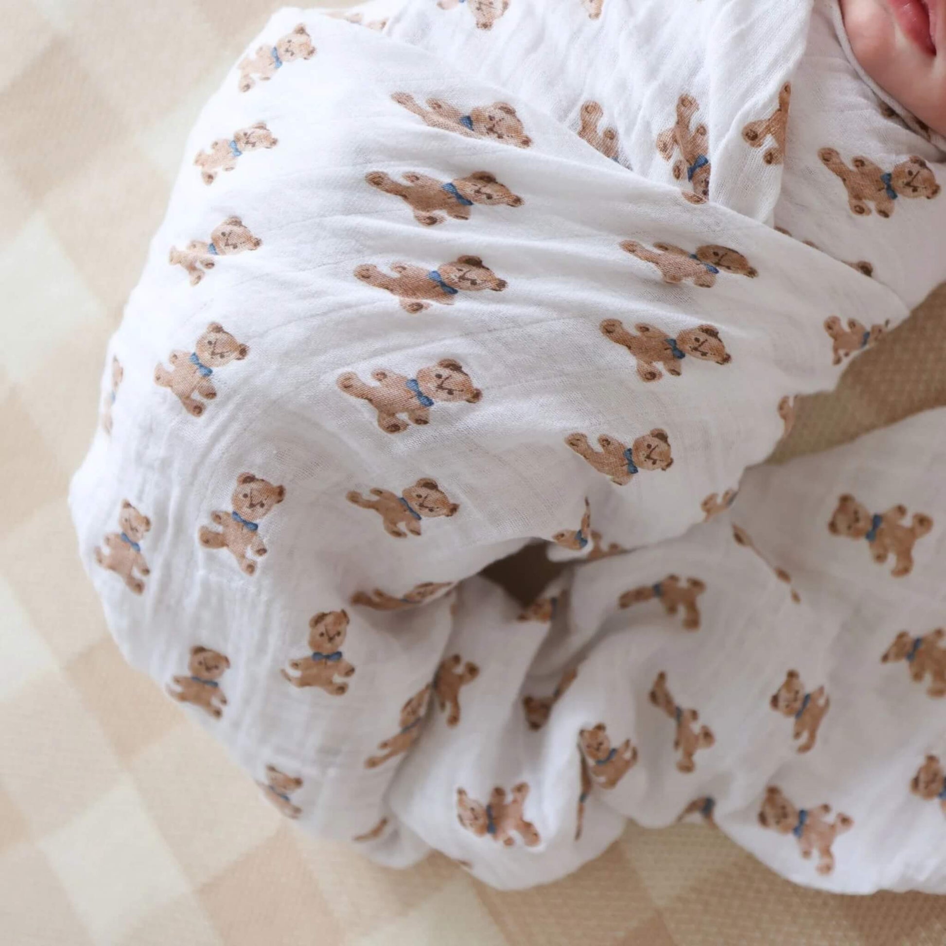 Close-up of white muslin fabric printed with small brown teddy bears wearing blue bows.