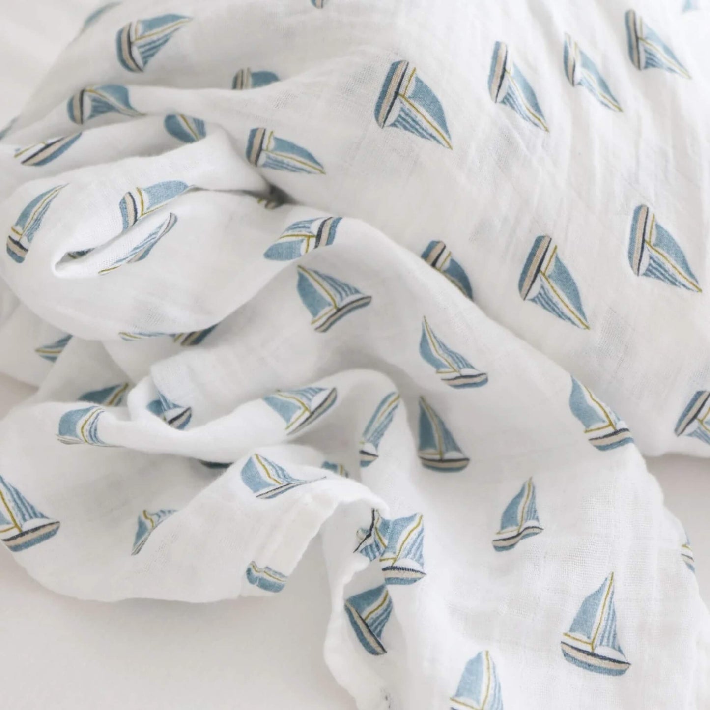 Close-up of soft muslin fabric patterned with small blue sailboats on a white background.