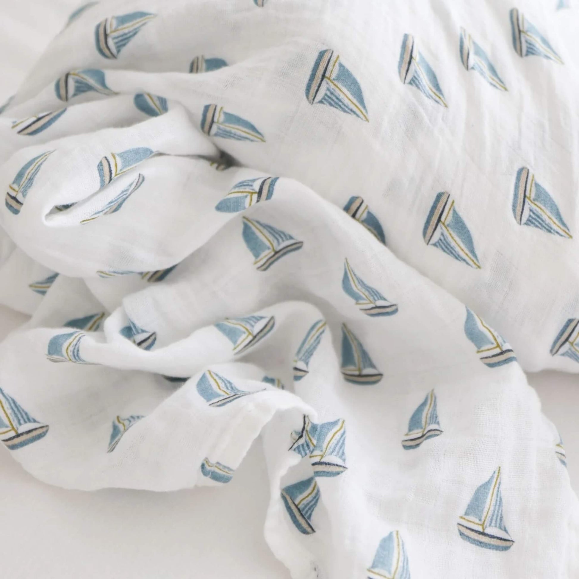 Close-up of soft muslin fabric patterned with small blue sailboats on a white background.