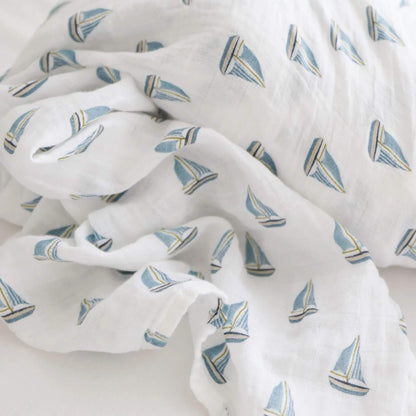 Close-up of soft muslin fabric patterned with small blue sailboats on a white background.