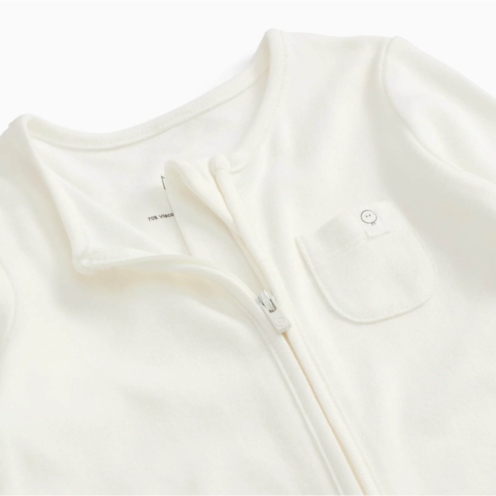 A close-up of a white baby sleepsuit showing the soft neckline, concealed zip and small chest pocket.