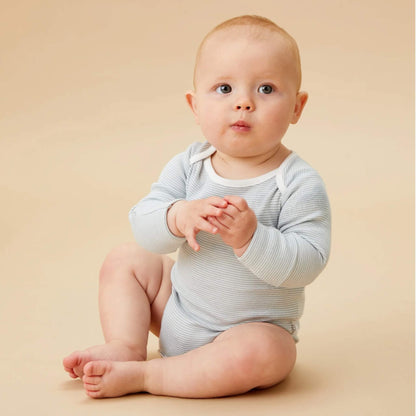 A baby sitting on a neutral backdrop wearing a blue striped long sleeve bodysuit, with hands together and looking slightly upward.