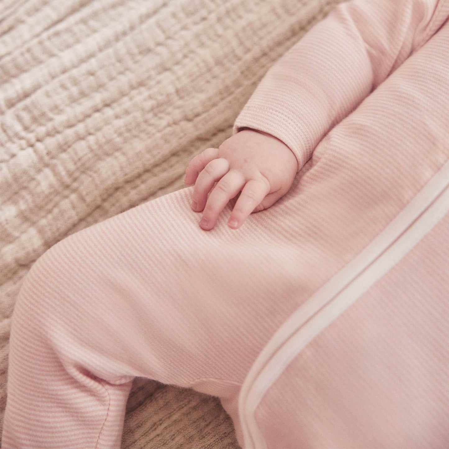 A close-up of a baby’s leg in a pink striped sleepsuit, showing the smooth fabric texture and long concealed zip.