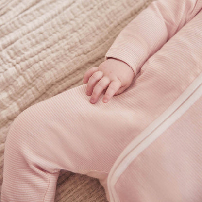 A close-up of a baby’s leg in a pink striped sleepsuit, showing the smooth fabric texture and long concealed zip.