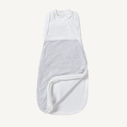 A newborn swaddle bag in grey shown partially unzipped at the bottom, revealing the soft inner lining and wrap-style chest panel with poppers.