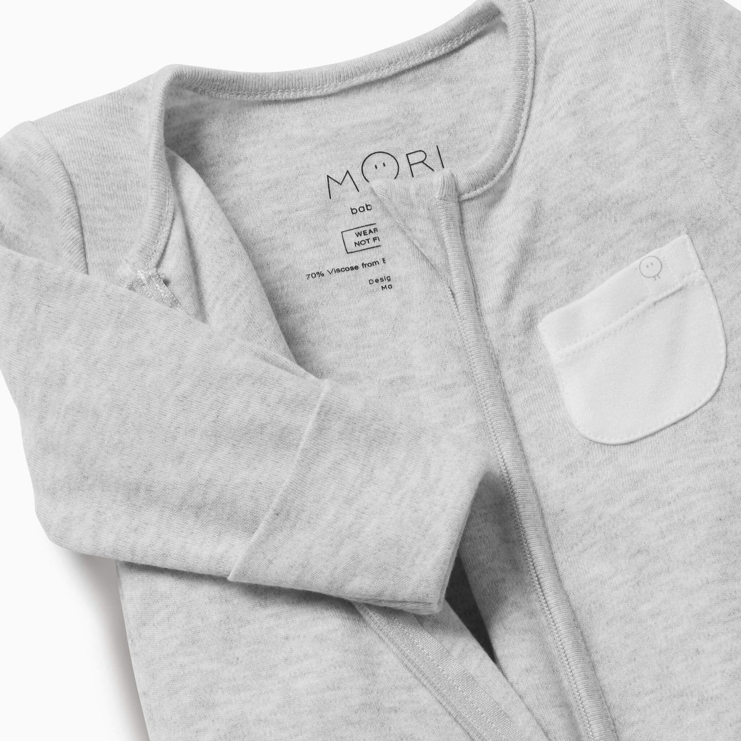 A close-up of a grey baby sleepsuit showing the soft neckline, concealed zip and small white chest pocket.