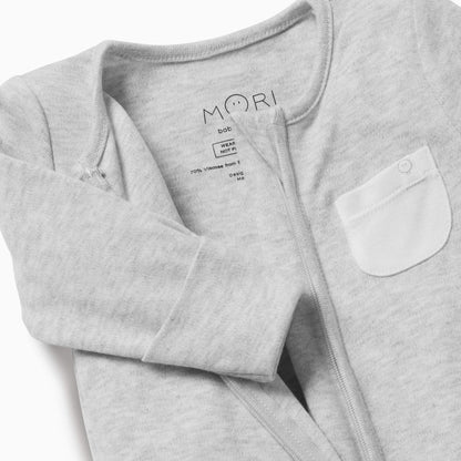 A close-up of a grey baby sleepsuit showing the soft neckline, concealed zip and small white chest pocket.