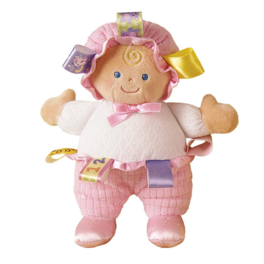 Mary Meyer Taggies Baby Doll soft toy with a pink bonnet, white knitted top, pink quilted trousers and satin ribbons around the head and waist.