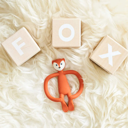 Fox-shaped baby teether placed on a fluffy surface beside wooden blocks spelling out the word ‘FOX’.
