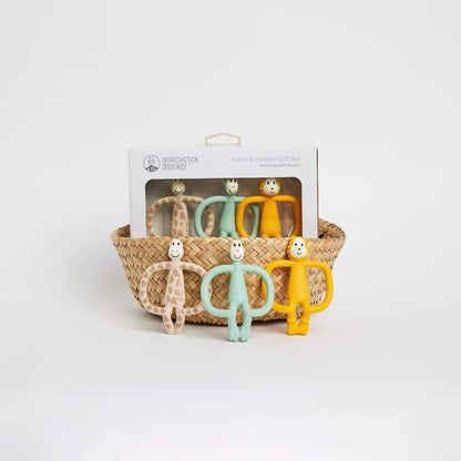 A woven basket containing a boxed set of three silicone animal-shaped teethers, with the three loose teethers positioned standing in front of the basket.
