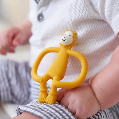 A yellow lion teether resting on a baby’s leg, showing the flexible looped handles and small textured mane.