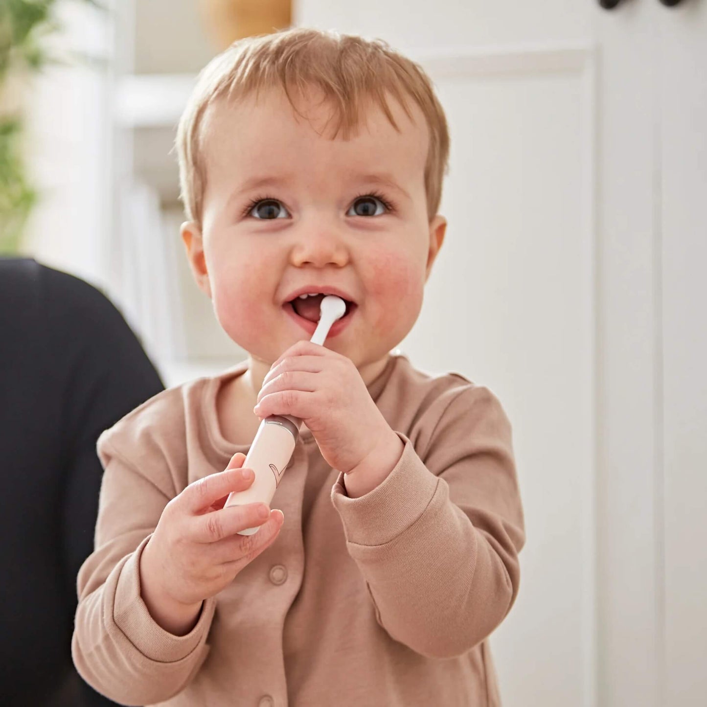 Baby holding a small electric toothbrush with rounded brush head designed for gentle brushing of emerging teeth.