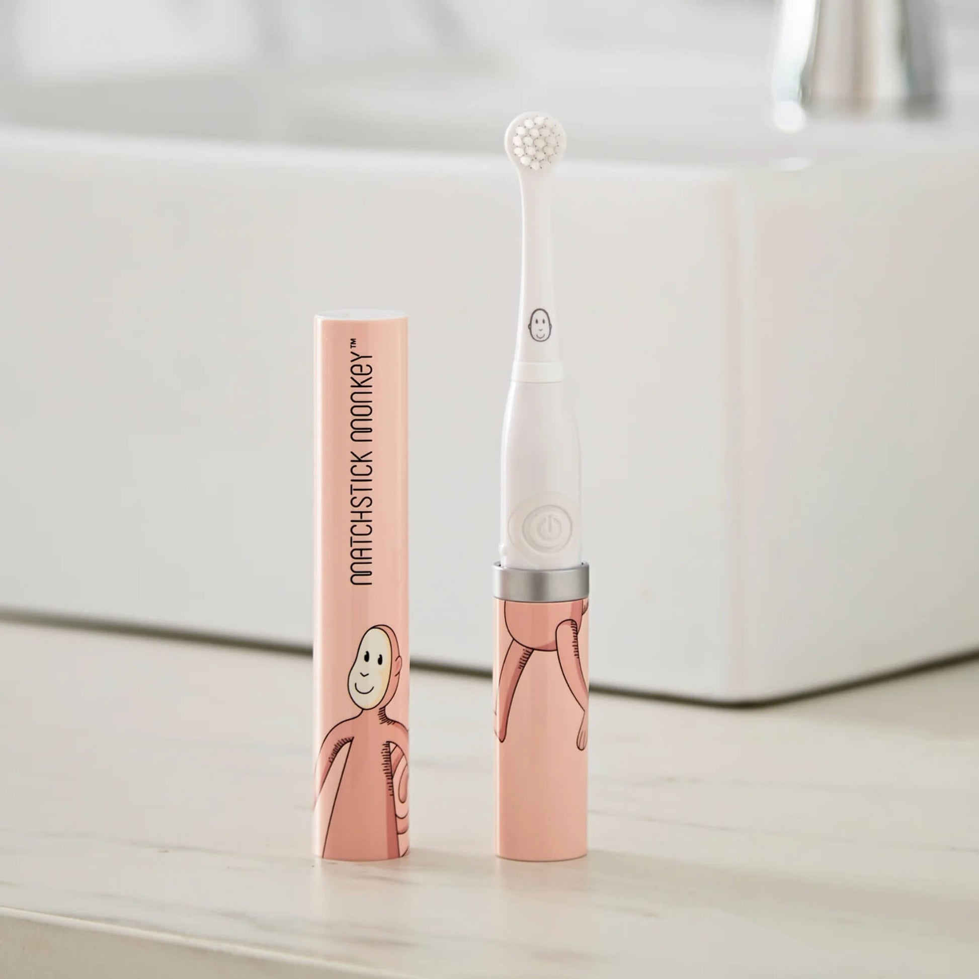 Electric baby toothbrush with small soft bristle head standing upright beside illustrated protective travel case on a bathroom counter.
