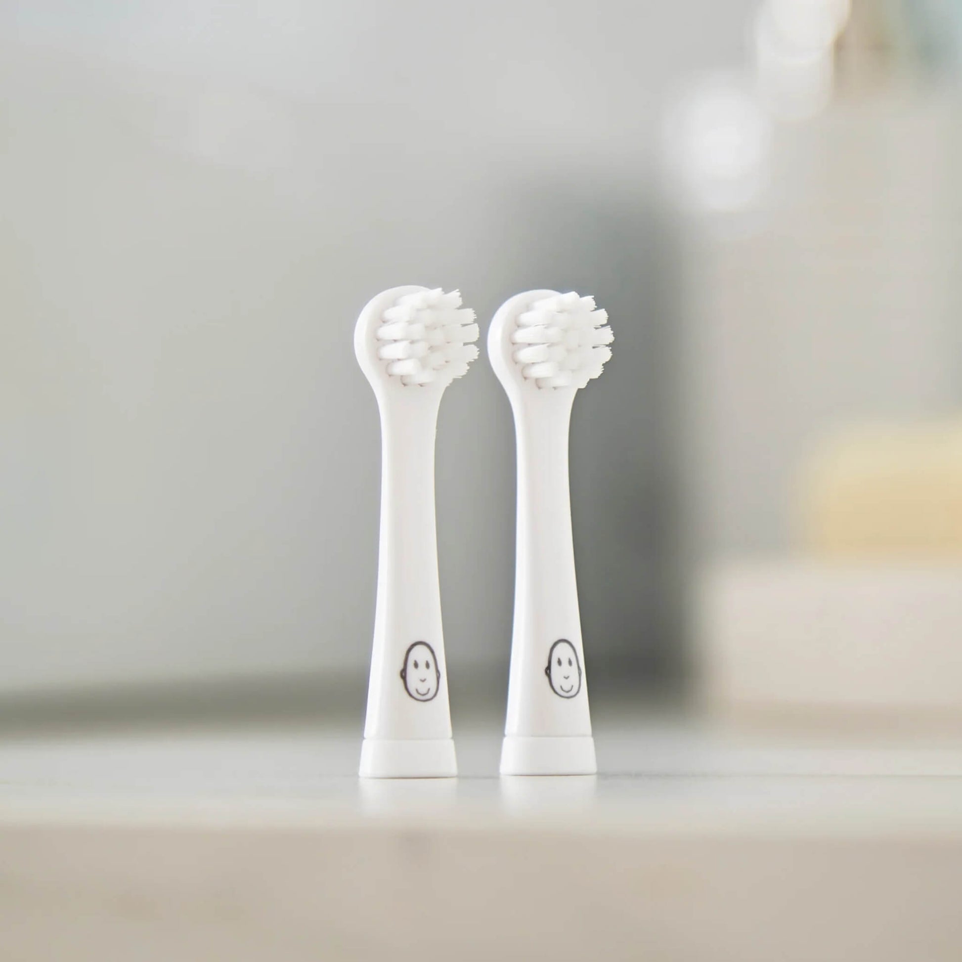 Close-up of two replacement toothbrush heads standing together on a clean bathroom surface, with soft lighting and a blurred background.
