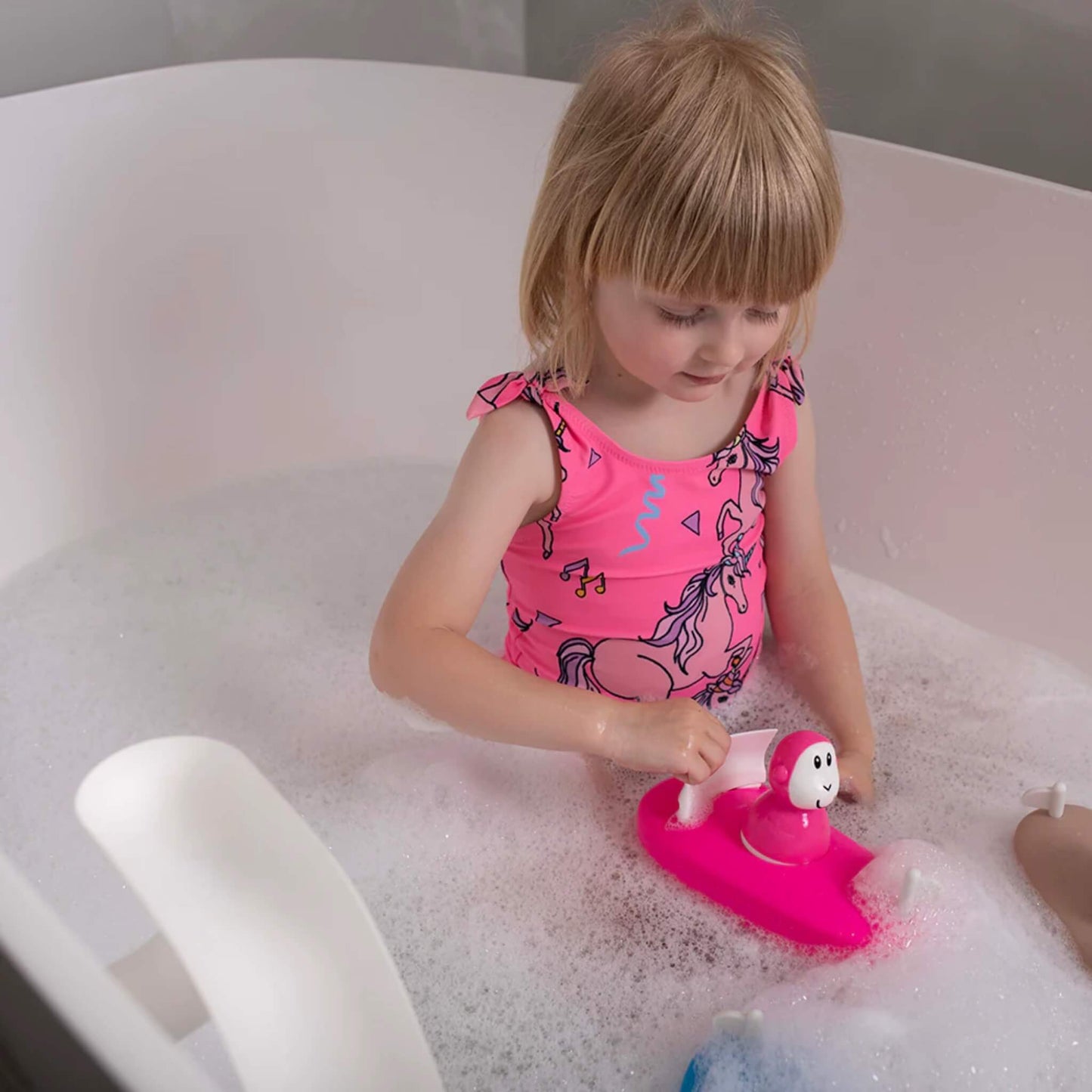 Young child sitting in a bubble bath holding the pink boat toy while interacting with the removable character.