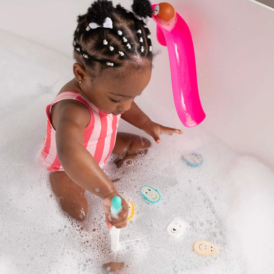 A toddler sitting in a bubble bath using the fishing rod to catch one of the floating character pieces.
