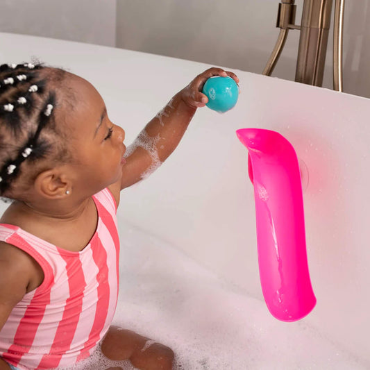 Young child sitting in a bubble-filled bath and holding a turquoise animal ball above a pink curved slide attached to the bath wall.