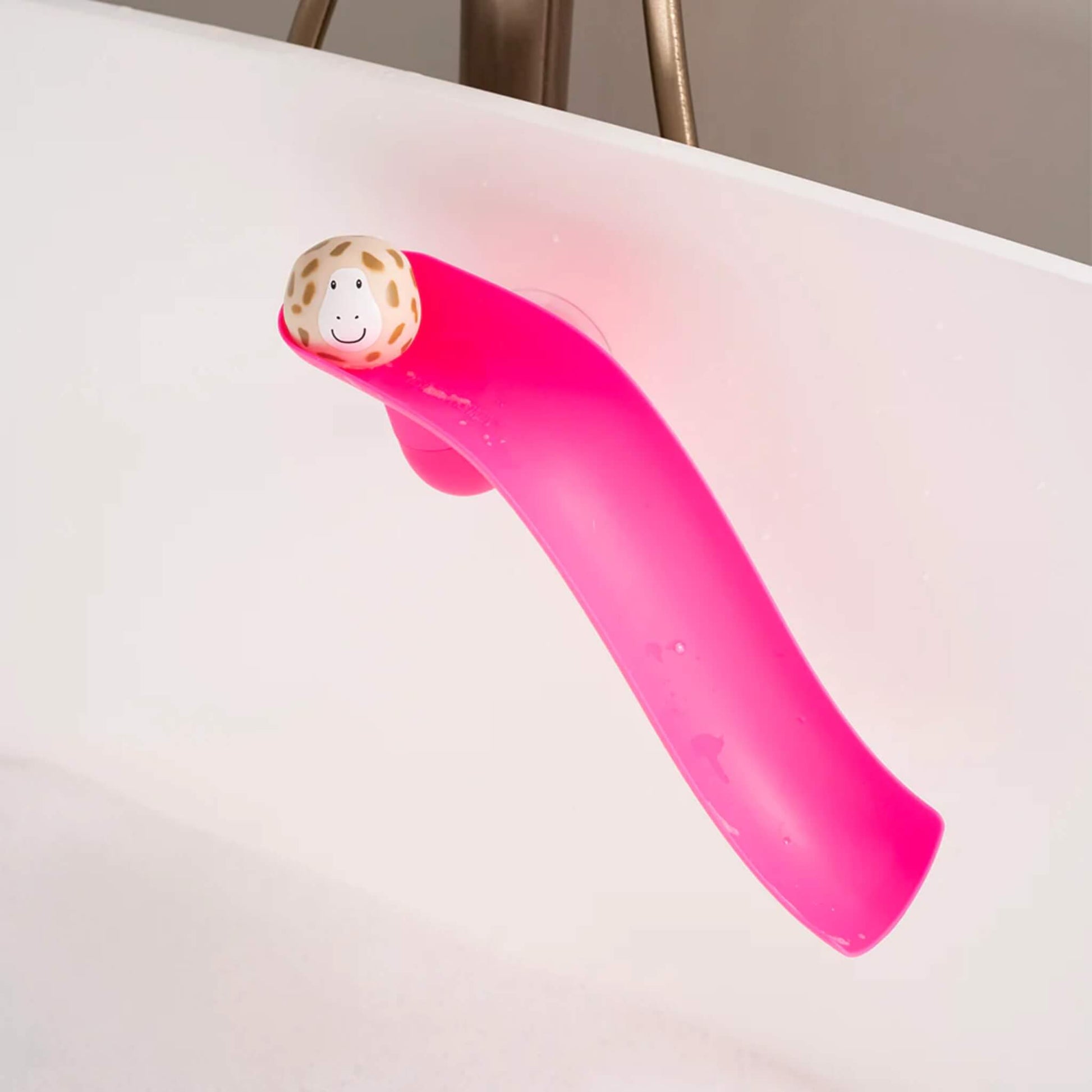 Pink curved silicone slide toy attached to the bath wall with a single beige animal ball resting at the top of the slide.
