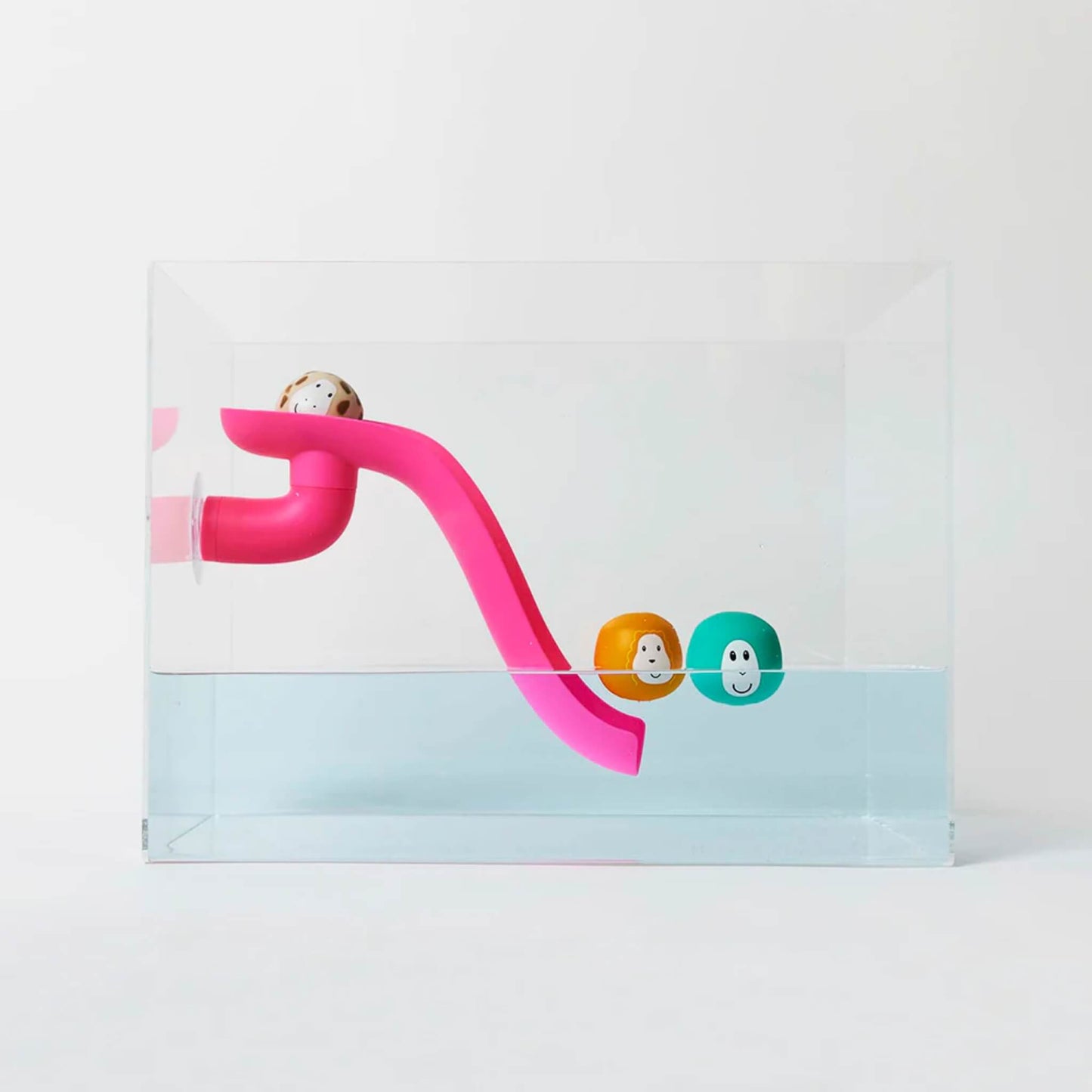Pink curved bath slide positioned inside a clear water tank with three floating animal character balls resting near the slide in the water.
