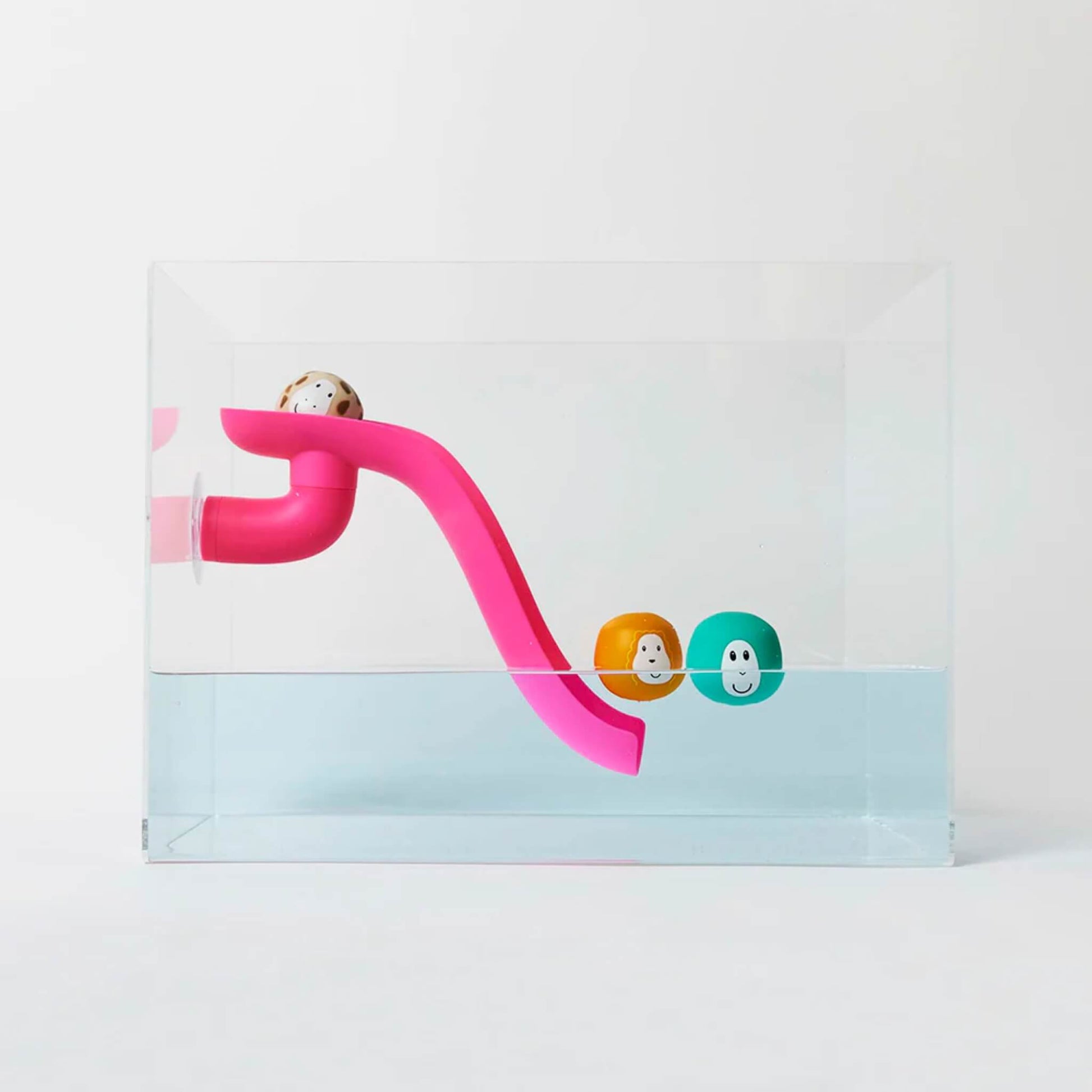 Pink curved bath slide positioned inside a clear water tank with three floating animal character balls resting near the slide in the water.