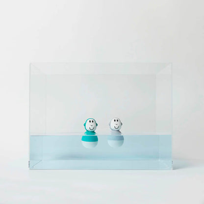 Two wobbling bath toys floating inside a clear water tank, with their rounded bases bobbing gently on the surface.