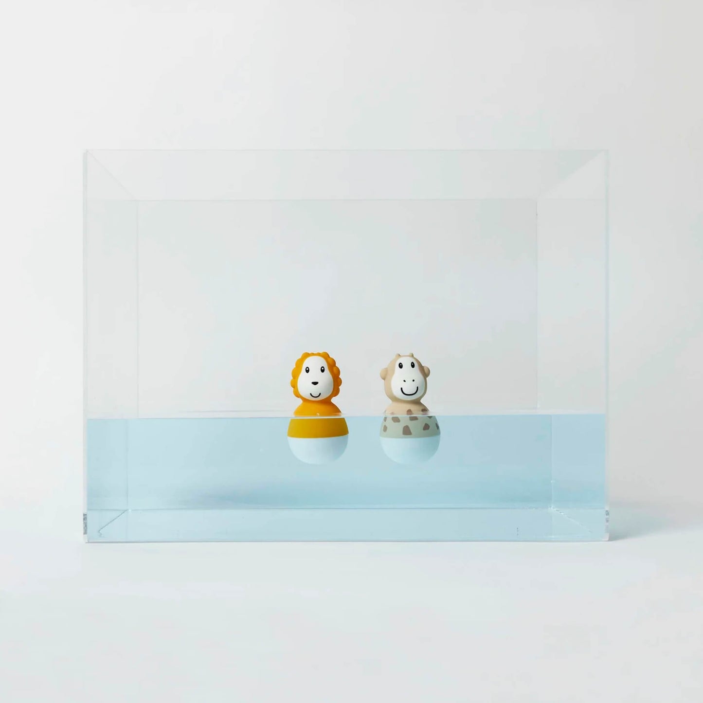 A lion and giraffe bath wobbler floating upright inside a clear water tank against a clean white backdrop.