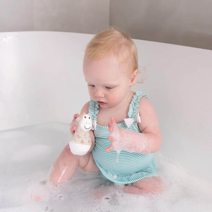 A baby sitting in a bubble bath holding a giraffe design bath wobbler with foam on their hands.