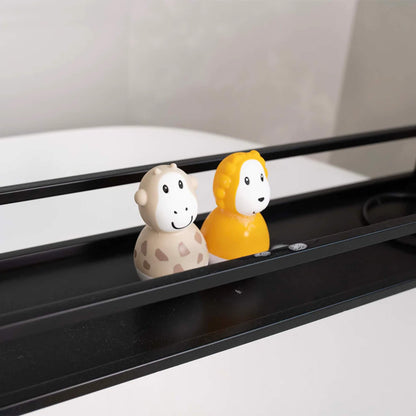 A lion and giraffe bath wobbler placed on a black metal bath caddy shelf beside each other.