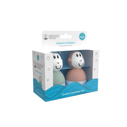 Packaging box holding two pastel wobbling bath toys, one mint green and one dusty pink, visible through a front window with blue wave graphics and small icons printed around the sides.