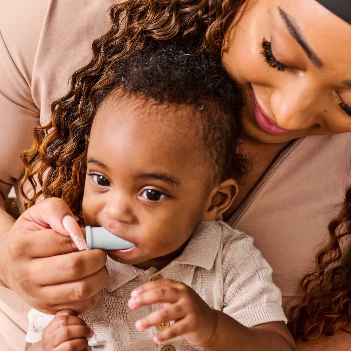 A mother gently brushing her baby’s first teeth with a soft silicone finger toothbrush.