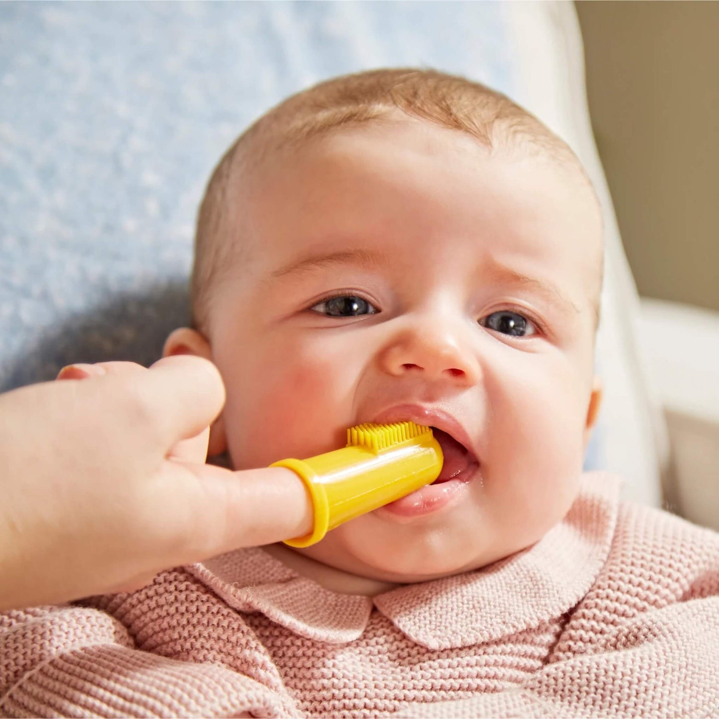Baby chewing on a yellow silicone finger toothbrush designed to massage sore teething gums.