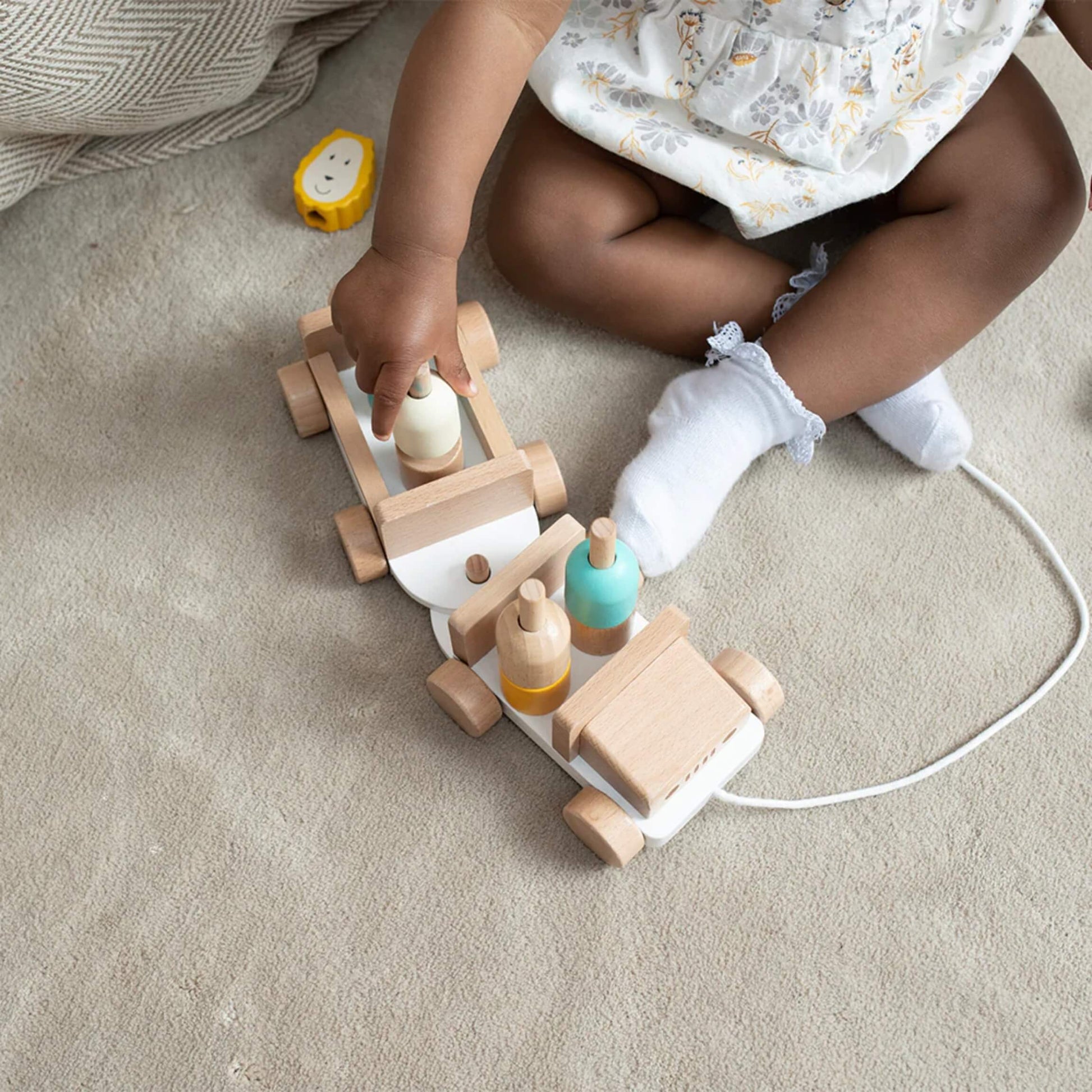 Baby sitting on a textured blanket, reaching for the animal figures while the wooden safari jeep sits on the floor nearby.