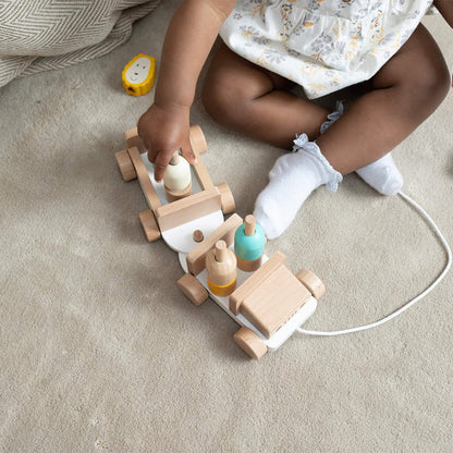 Baby sitting on a textured blanket, reaching for the animal figures while the wooden safari jeep sits on the floor nearby.