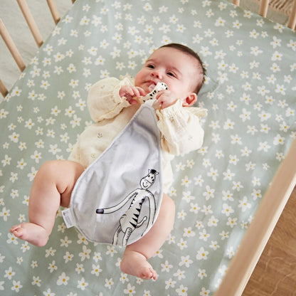 Baby lying in a cot holding the zebra-shaped soother and gripping the grey comforter cloth during play.
