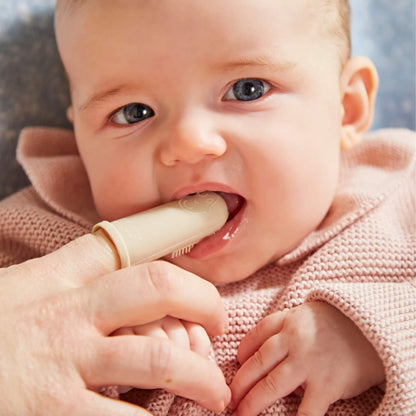 A close-up of a baby biting on a silicone finger toothbrush while an adult supports it with their hand.