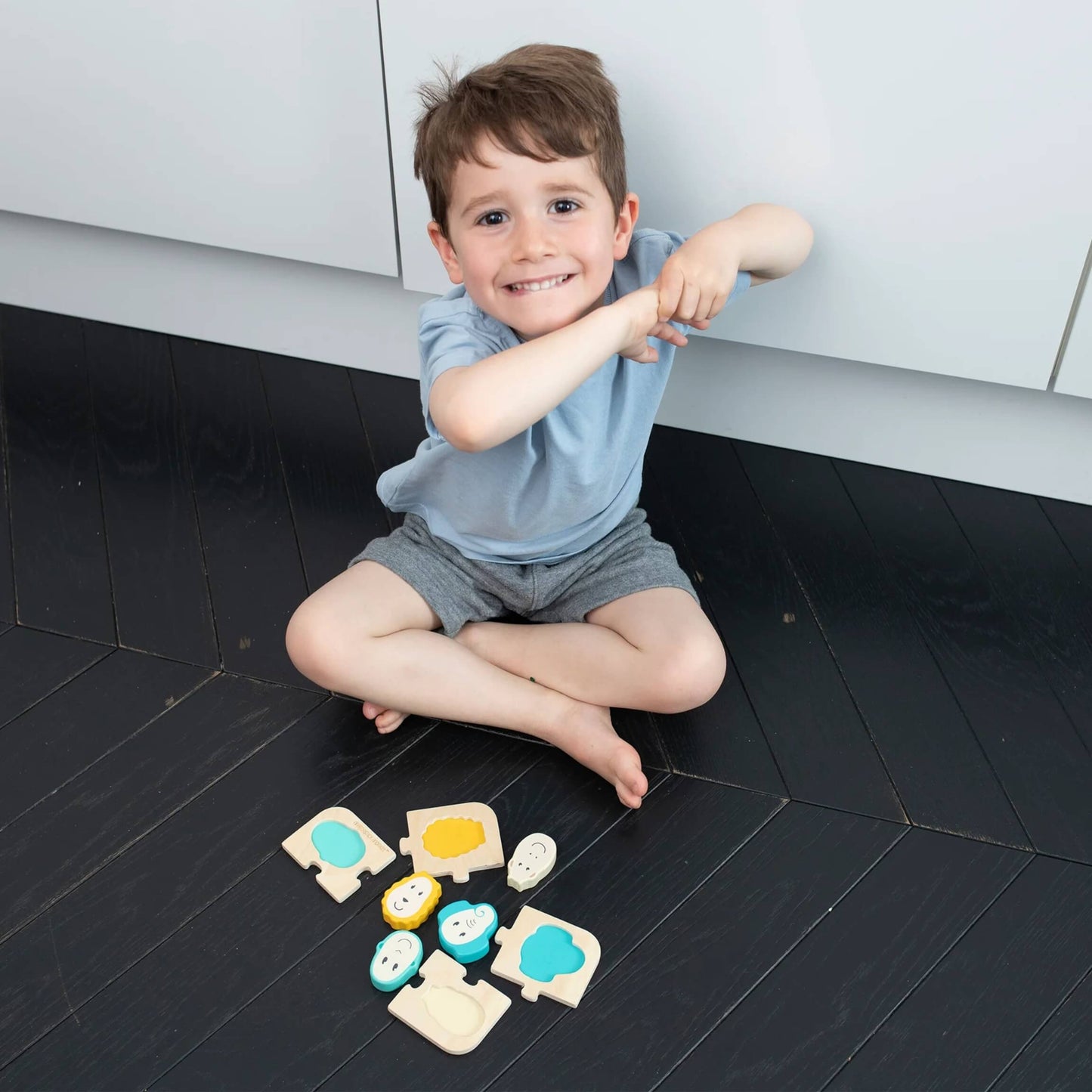 A young child sitting on a dark wood floor playing with the wooden animal puzzle pieces arranged around them.
